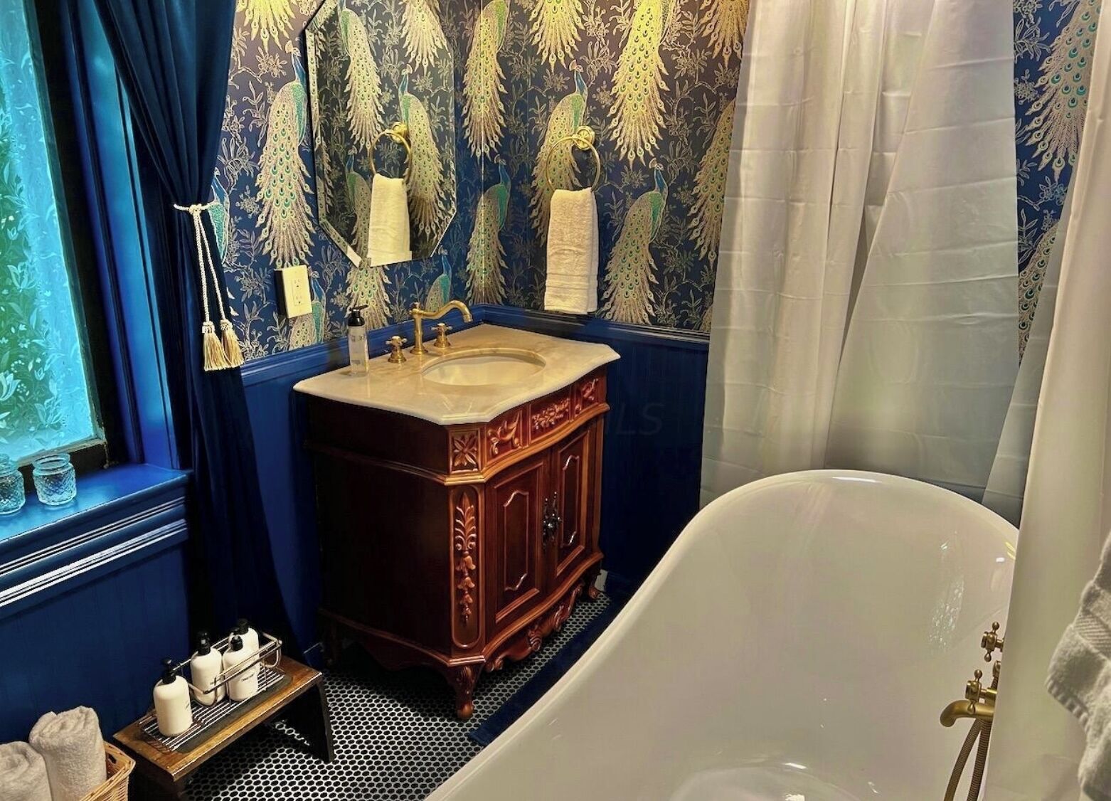 A bathroom with a freestanding bathtub, a wooden vanity with a sink, and a peacock-themed wallpaper.