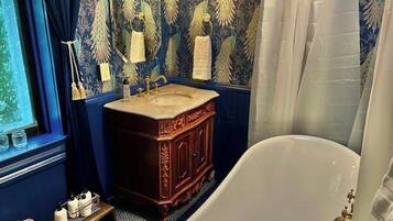 A bathroom with a freestanding bathtub, a wooden vanity with a sink, and a peacock-themed wallpaper.