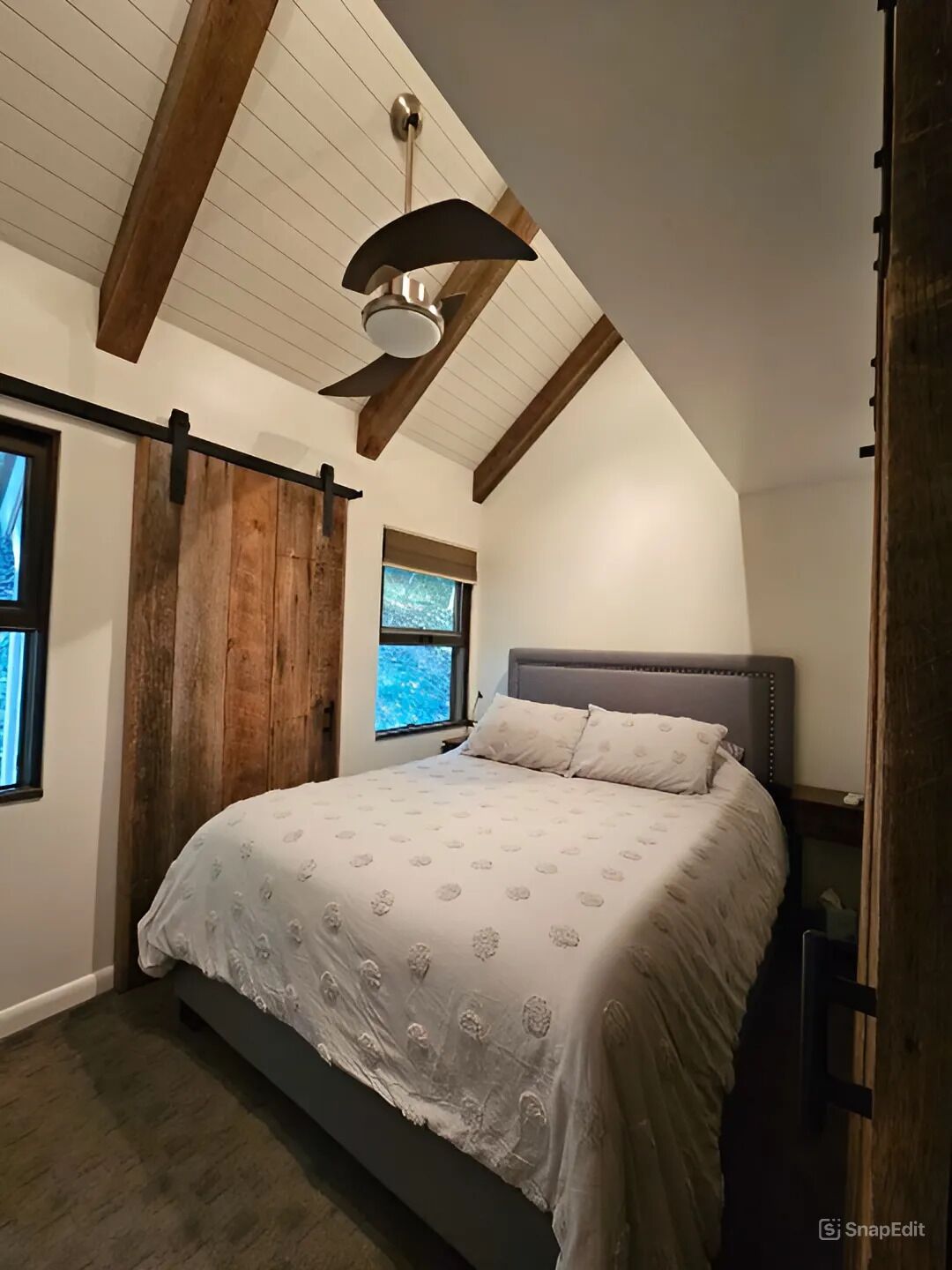 Une chambre à coucher avec un lit, des poutres en bois au plafond, un ventilateur de plafond et une fenêtre.