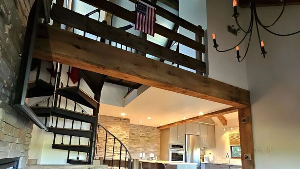 A spacious loft with a wooden staircase, a kitchen area, and a seating area with a glass coffee table. - Lake Loft at Deep Creek Lake (Oakland)