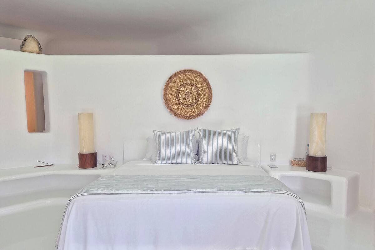 A minimalist bedroom with a large bed, two bedside tables, and a decorative wall hanging.