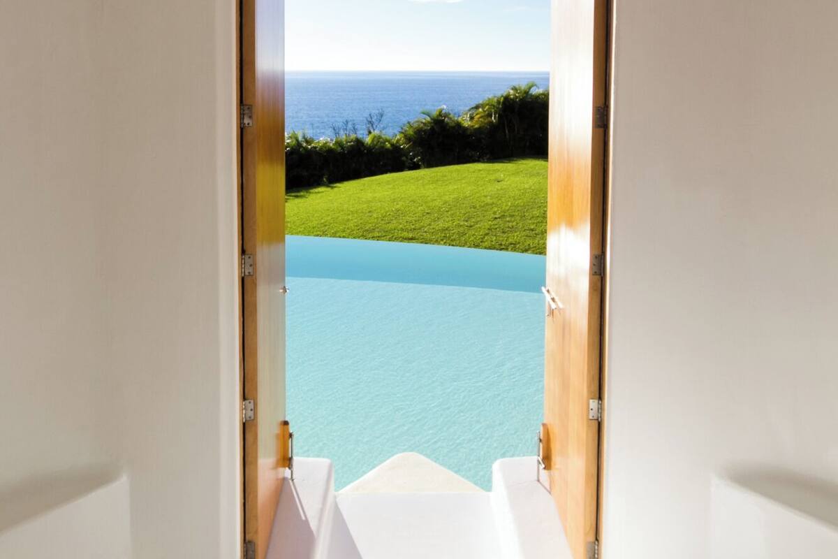 A doorway leading to a pool with a clear view of the ocean and a grassy area.