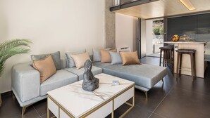 A modern living room with a sectional sofa, a marble coffee table, and a kitchen area with a bar and stools. - Agrimi Luxury Suite with Private Pool  (Sfakia)