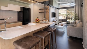 A modern kitchen with a central island, bar stools, a flat-screen TV, and a view of the outdoors.