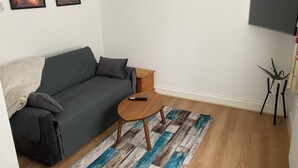A modern living room with a grey sofa, a small wooden side table, a blue and white patterned rug, and two framed pictures on the wall. - Slough - Sleeps 3 - Petfriendly - Riverside - Bay (Slough)