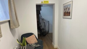 A hallway with a staircase, a black chair with a cushion, a small table with a plant, and a framed picture on the wall. - Slough - Sleeps 3 - Petfriendly - Riverside - Bay (Slough)
