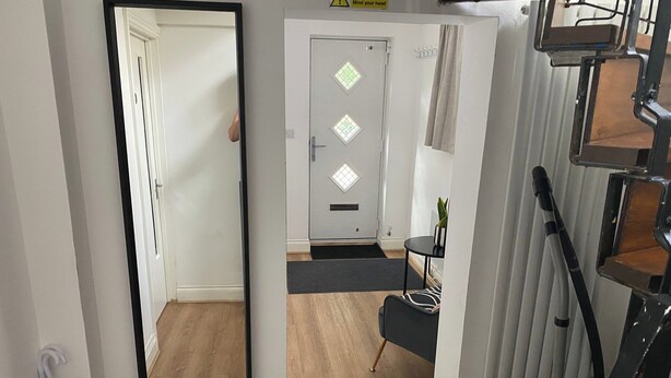 A hallway with a mirror, a door with diamond-shaped windows, a small table with a plant, and a vacuum cleaner. - Slough - Sleeps 3 - Petfriendly - Riverside - Bay (Slough)