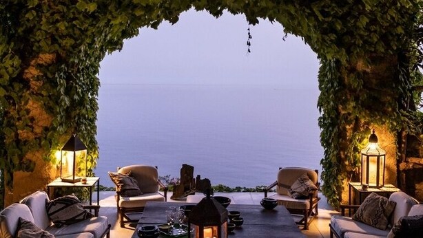 An outdoor seating area with tables and chairs, a lantern, and a view of the sea. - Villa Luna by MyVillaCollection (Maiori)