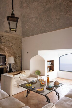 A living room with a sofa, a coffee table with food, a lamp, and a bookshelf.