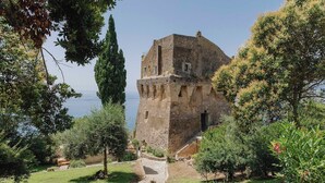 A stone building with a tower, surrounded by trees and a clear sky. - Villa Fortino by MyVillaCollection (Maiori)