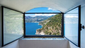A room with a large arched window overlooking a coastal landscape with mountains and a body of water. - Villa Fortino by MyVillaCollection (Maiori)