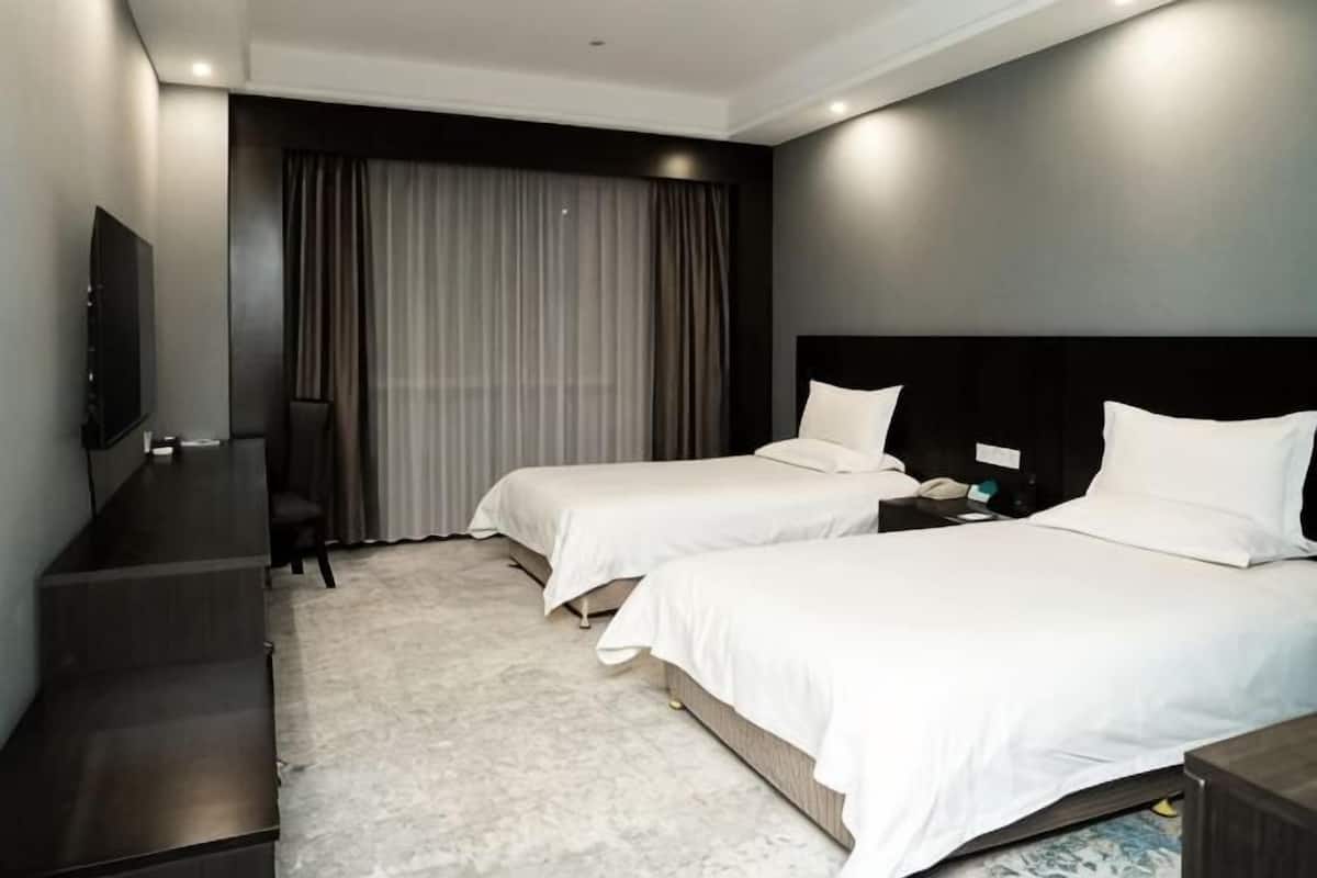A hotel room with two beds, a desk, a TV, and a large window with curtains.