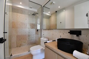 Ein modernes Badezimmer mit einer gläsernen Dusche, einer weißen Toilette, einem schwarzen Waschbecken und einem Spiegel darüber.