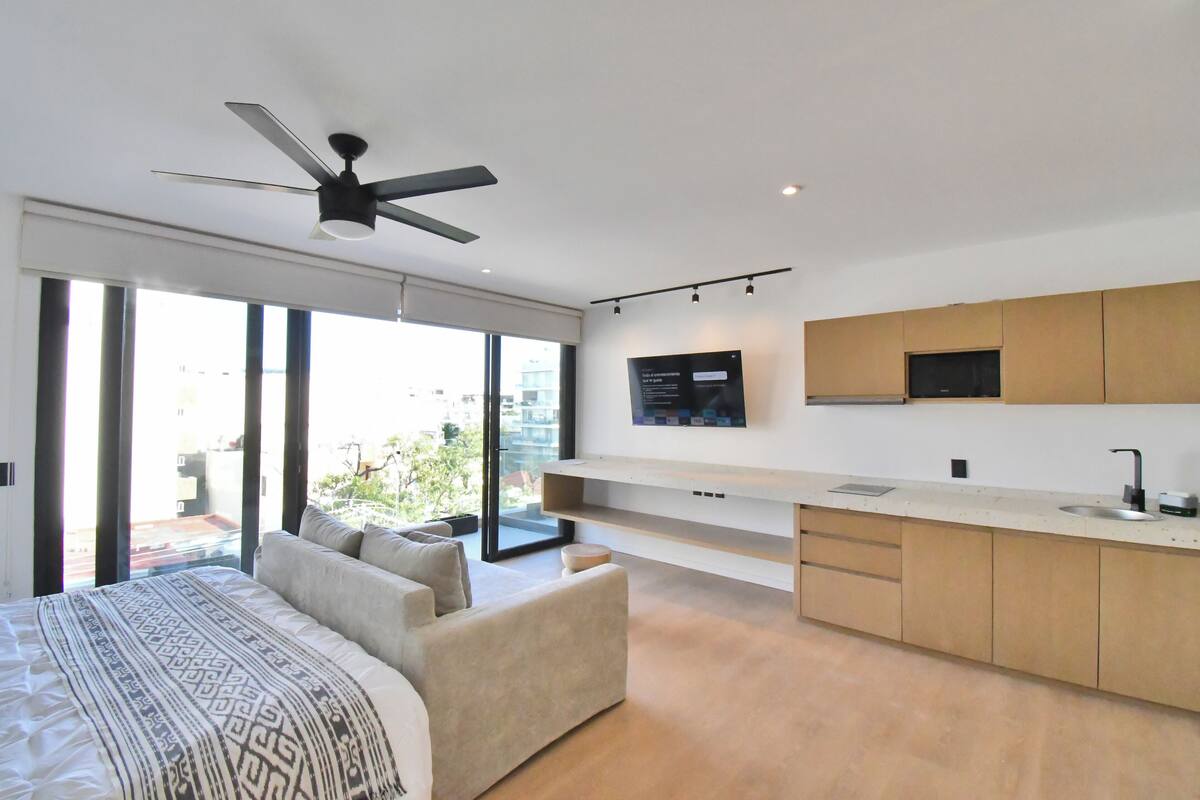 A modern bedroom with a large bed, a sofa, and a ceiling fan.