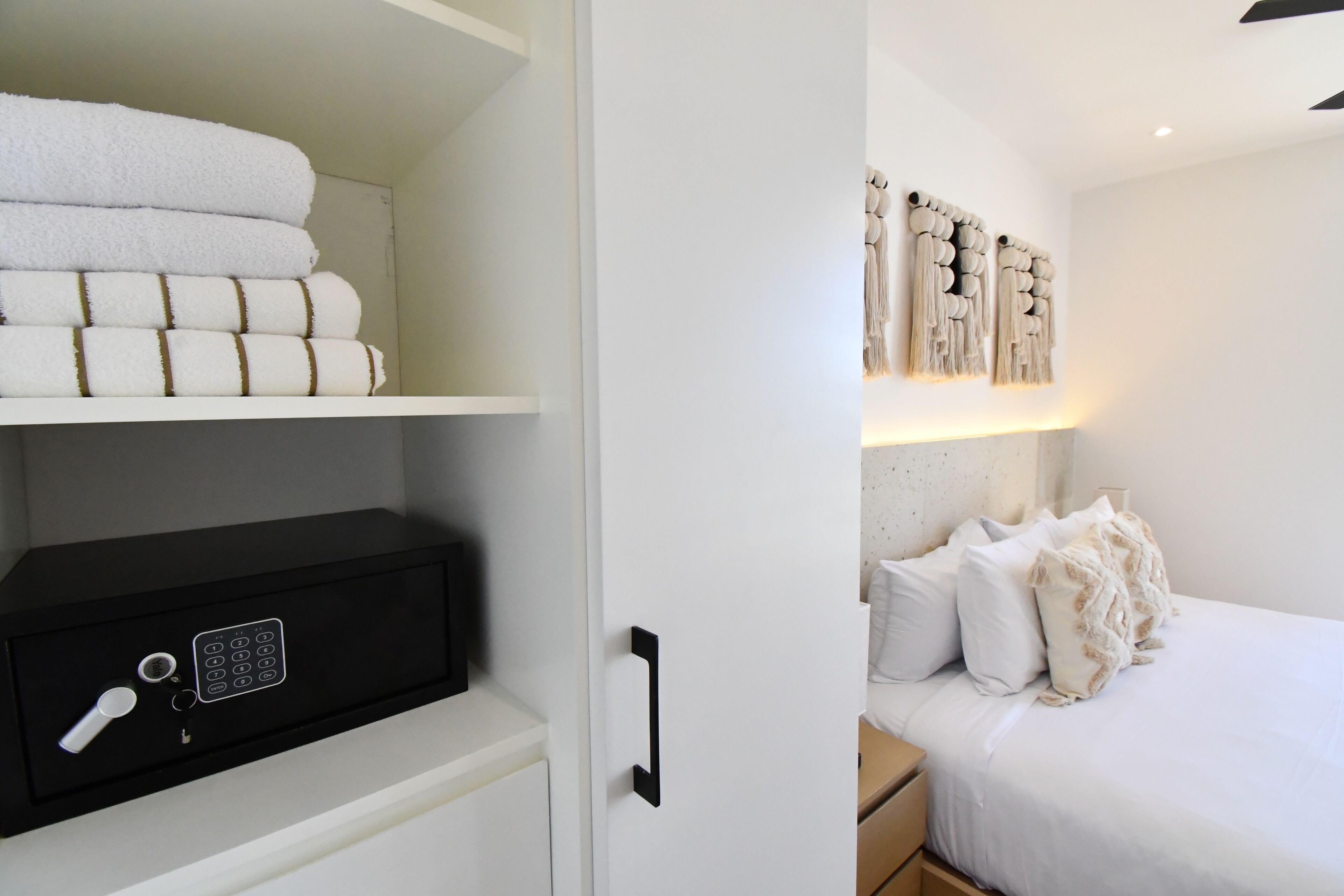 A hotel room with a neatly organized closet containing folded towels and a black safe.