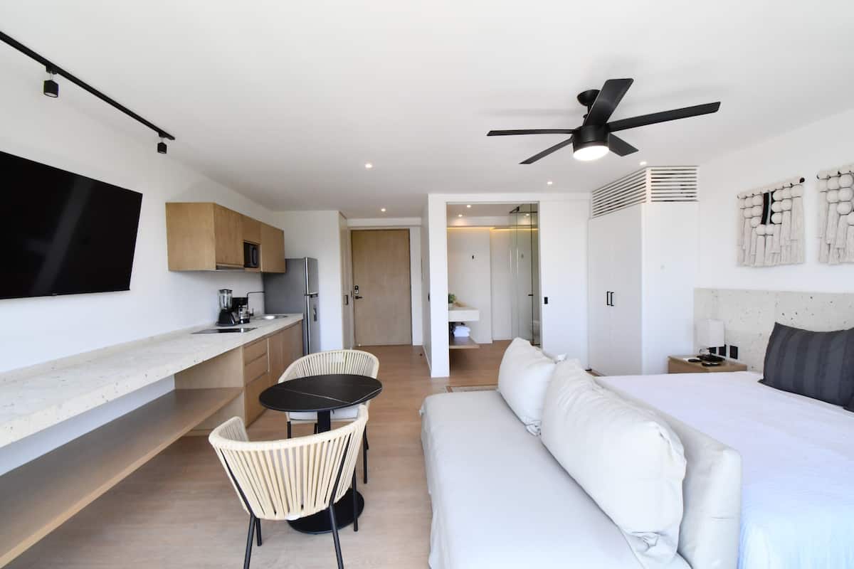 A modern hotel room with a kitchenette, a dining area, a bed, and a ceiling fan.