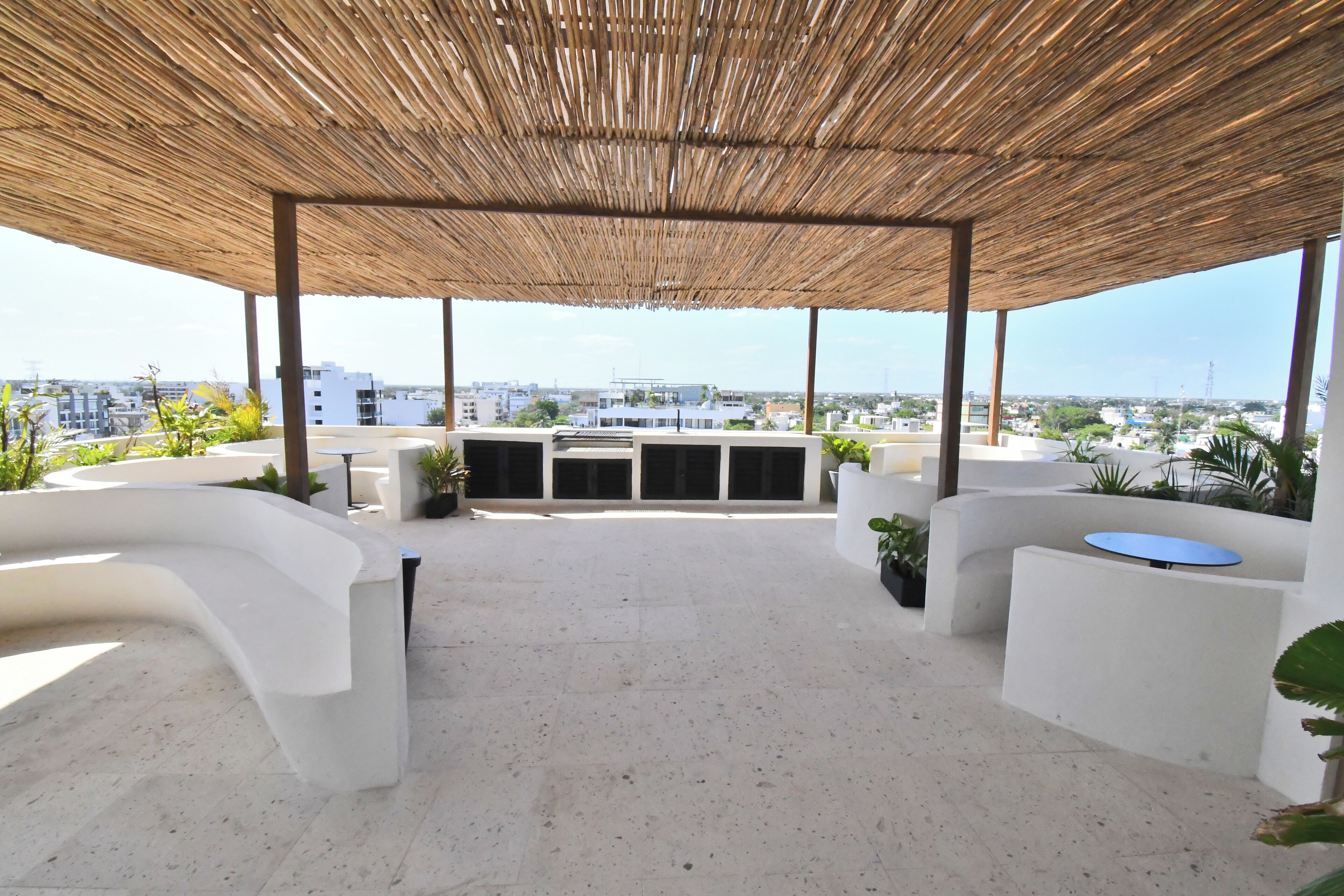 An outdoor terrace with a thatched roof, white stone flooring, and seating areas.
