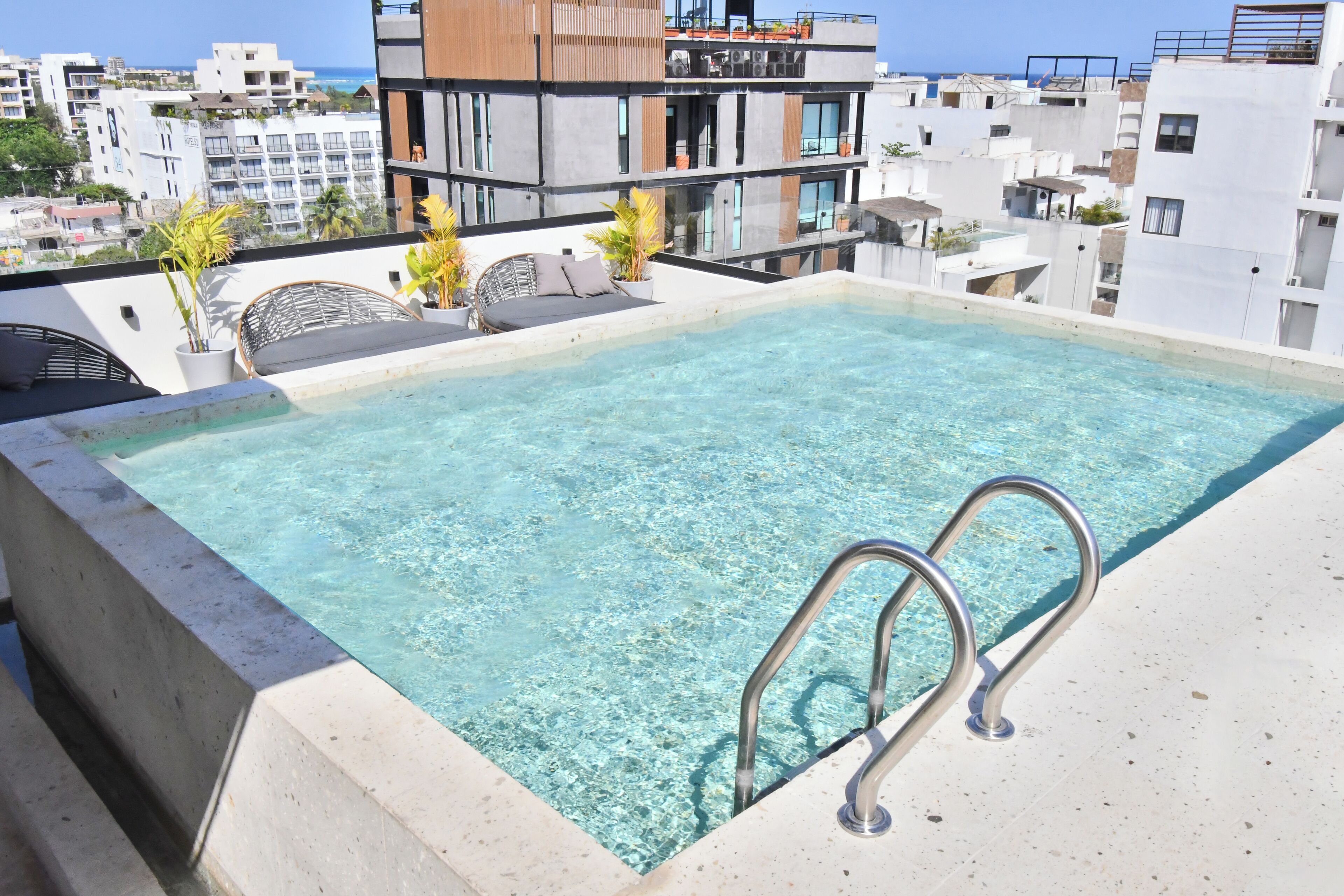 A rooftop infinity pool with clear water, surrounded by modern buildings and a view of the sea.