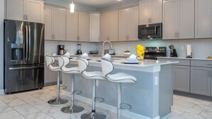 Une cuisine moderne dotée d’appareils électroménagers en acier inoxydable, de tabourets de bar blancs et de meubles de rangement gris.