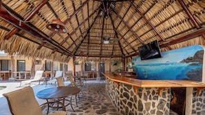 A thatched-roof outdoor seating area with stone flooring, a wooden bar with a stone counter, and a mural of a coastal scene. - Cozy Seaside AC Cabin, 300m from ocean, with pool (Provincia de Guanacaste)
