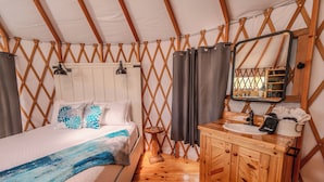 Una habitación con tienda de campaña, una cama, armarios de madera, un lavabo y un espejo.