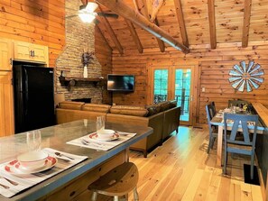 A cozy cabin interior with a stone fireplace, wooden walls, a dining area, and a living room with a sofa.
