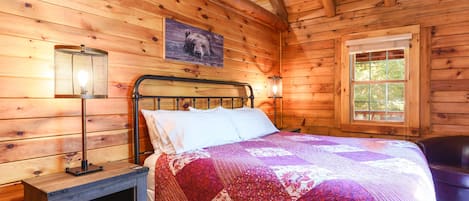 Un dormitorio de cabaña de madera con cama, mesita de noche, lámpara y ventana.