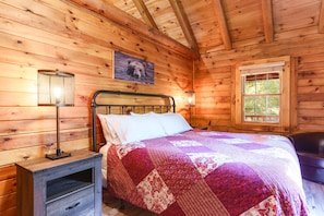 Un dormitorio de cabaña de madera con cama, mesita de noche, lámpara y ventana.