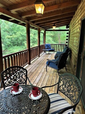 A wooden deck with a view of dense green foliage, two metal chairs, a table with two red cups, and a lantern hanging from the ceiling.