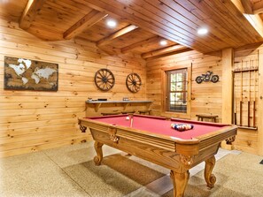 A wooden room with a pool table, two wooden walls, a window, and a motorcycle on the wall.