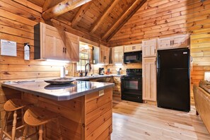 A wooden cabin kitchen with a central island, wooden cabinets, a black refrigerator, and a microwave.
