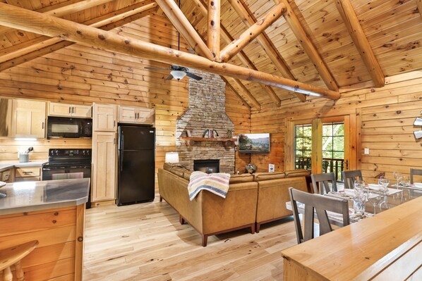 A log cabin interior with a kitchen, dining area, and fireplace.