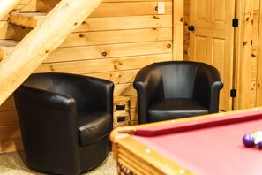 A wooden room with two black leather chairs and a pool table.