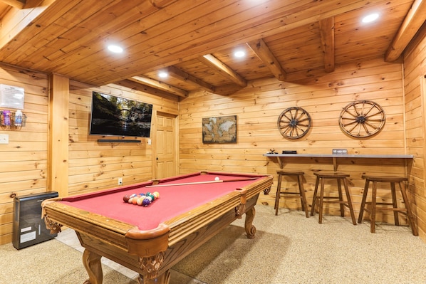 Una mesa de billar con taburetes, un televisor y paredes de madera.