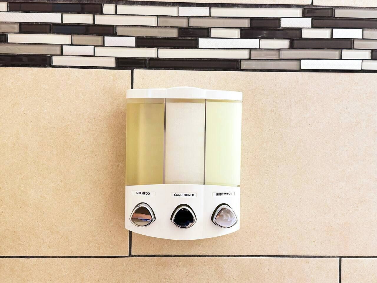 Douche bevestigd aan de muur met drie afzonderlijke bedieningen, gelabeld als 'shampoo', 'conditioner' en 'douchegel'.