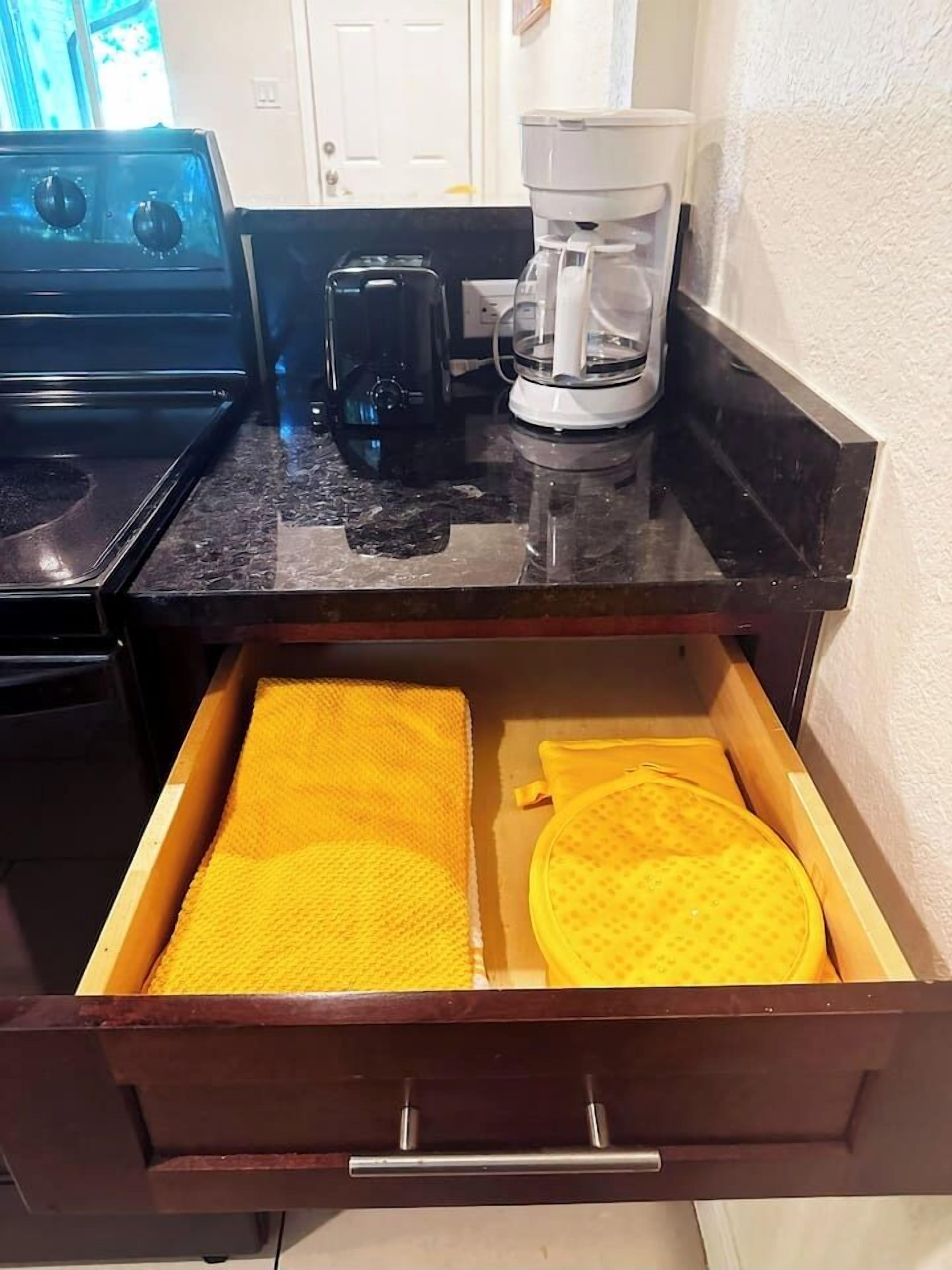 A kitchen with a stove, coffee maker, and a drawer with yellow kitchen towels.