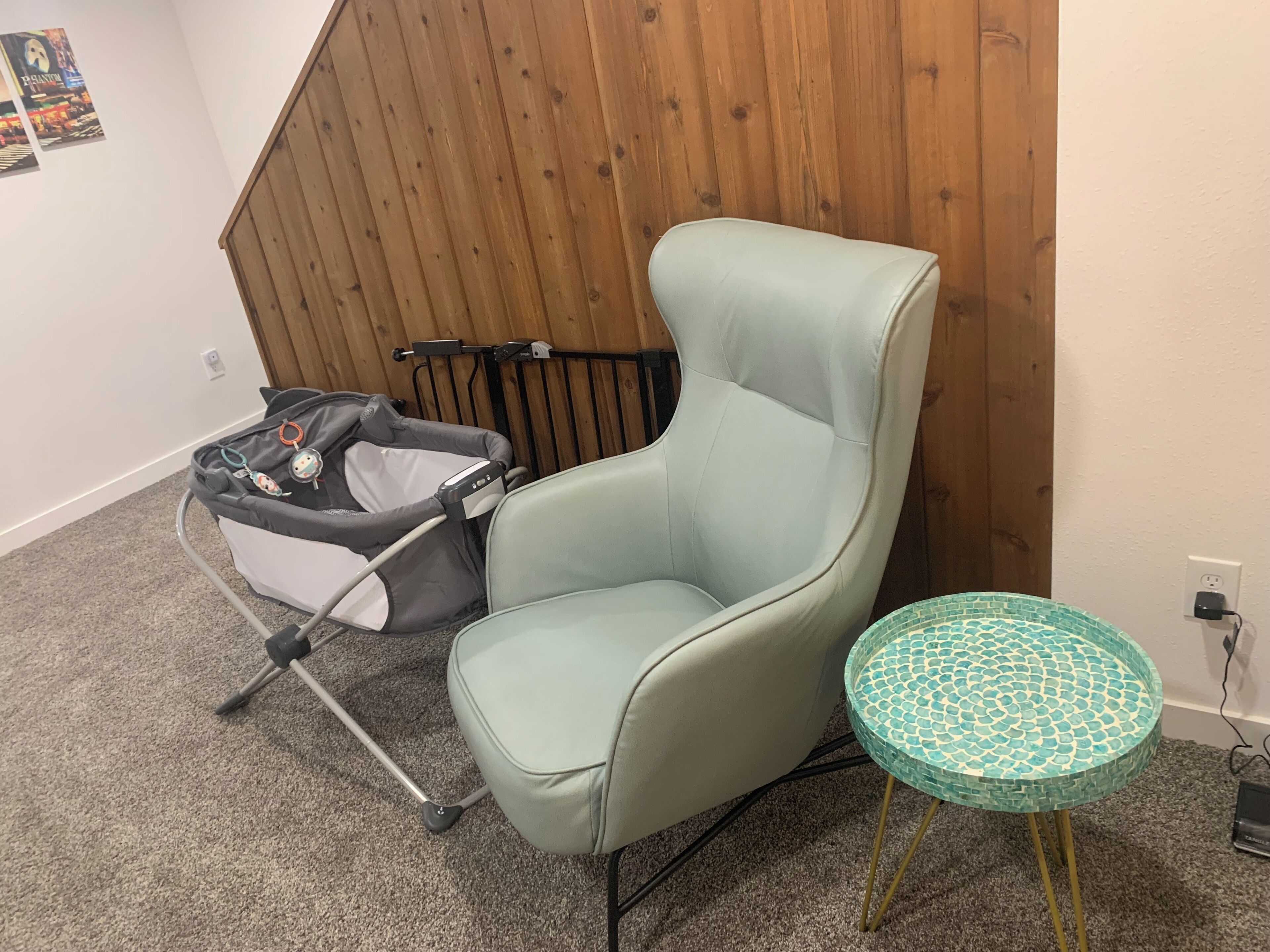 Une pièce avec une chaise vert clair, une petite table ronde dont le plateau est recouvert de mosaïques, et une poussette appuyée contre un mur en bois.