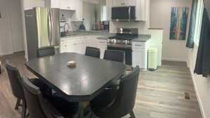 Une cuisine moderne avec des meubles blancs, des appareils en acier inoxydable et un coin repas comprenant une table et des chaises noires.