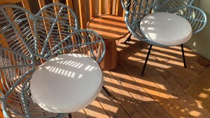 Une terrasse en bois avec deux tables rondes blanches et deux chaises en osier bleues.