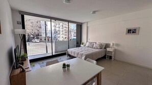 Una camera da letto moderna con una grande finestra, un letto, un comodino e una scrivania con una sedia.