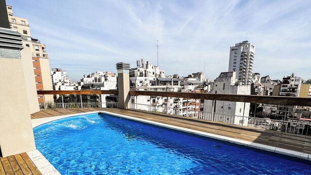 Una piscina sul tetto con un solarium in legno e vista sulla città.