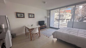 Una camera da letto con un letto, una televisione, una scrivania con sedie e una finestra vista edifici e alberi.