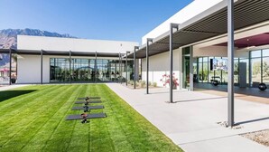 A modern building with a covered outdoor area, a grassy lawn, and exercise equipment. - Sophisticated Resort/WFA Amenity-Filled PS Home (Palm Springs)