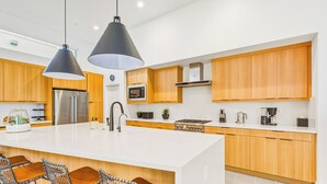 A modern kitchen with a large island, wooden cabinets, stainless steel appliances, and bar stools. - Sophisticated Resort/WFA Amenity-Filled PS Home (Palm Springs)
