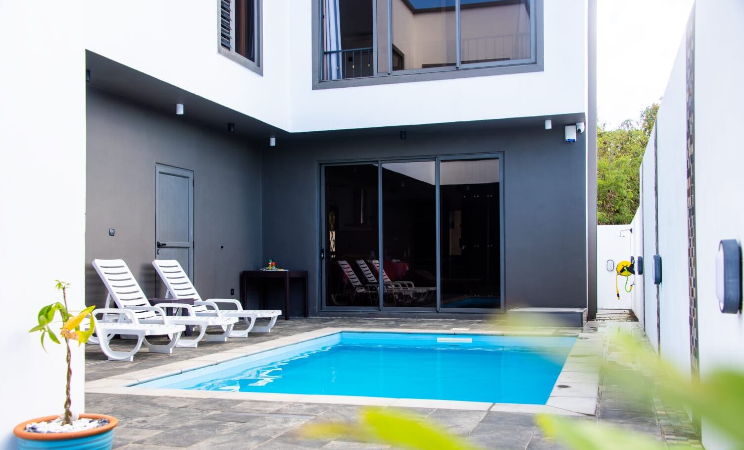 Una casa moderna con piscina, poltrone da relax bianche e una porta scorrevole in vetro che si apre su un portico coperto.
