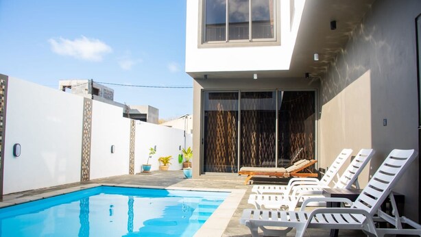 A modern outdoor pool area with white lounge chairs and a glass door leading to a covered patio.