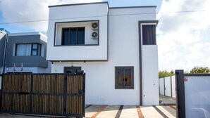 A modern two-story building with a flat roof, large windows, and a wooden fence.