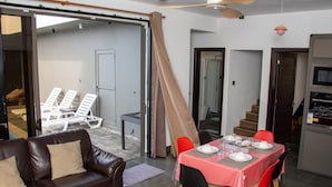 A dining area with a table set for four, a brown leather sofa, and a sliding glass door leading to a pool area with lounge chairs.