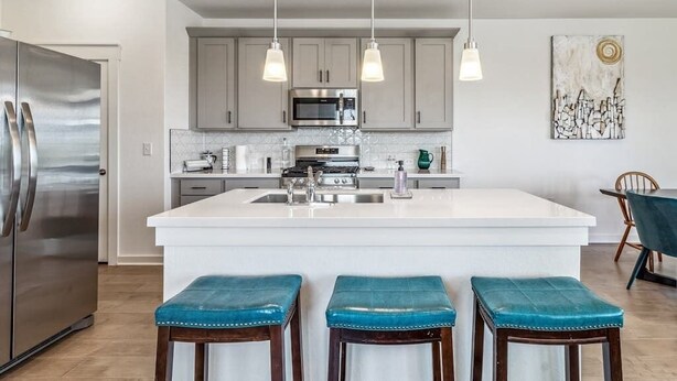 Een moderne keuken met een centraal eiland, roestvrijstalen apparatuur, hangende verlichting en een eethoek met tafel en stoelen.