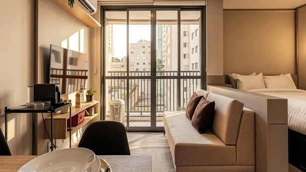 A modern hotel room with a bed, a sofa, a dining table, and a balcony with a view of buildings. - Xtay Vila Madalena (São Paulo)